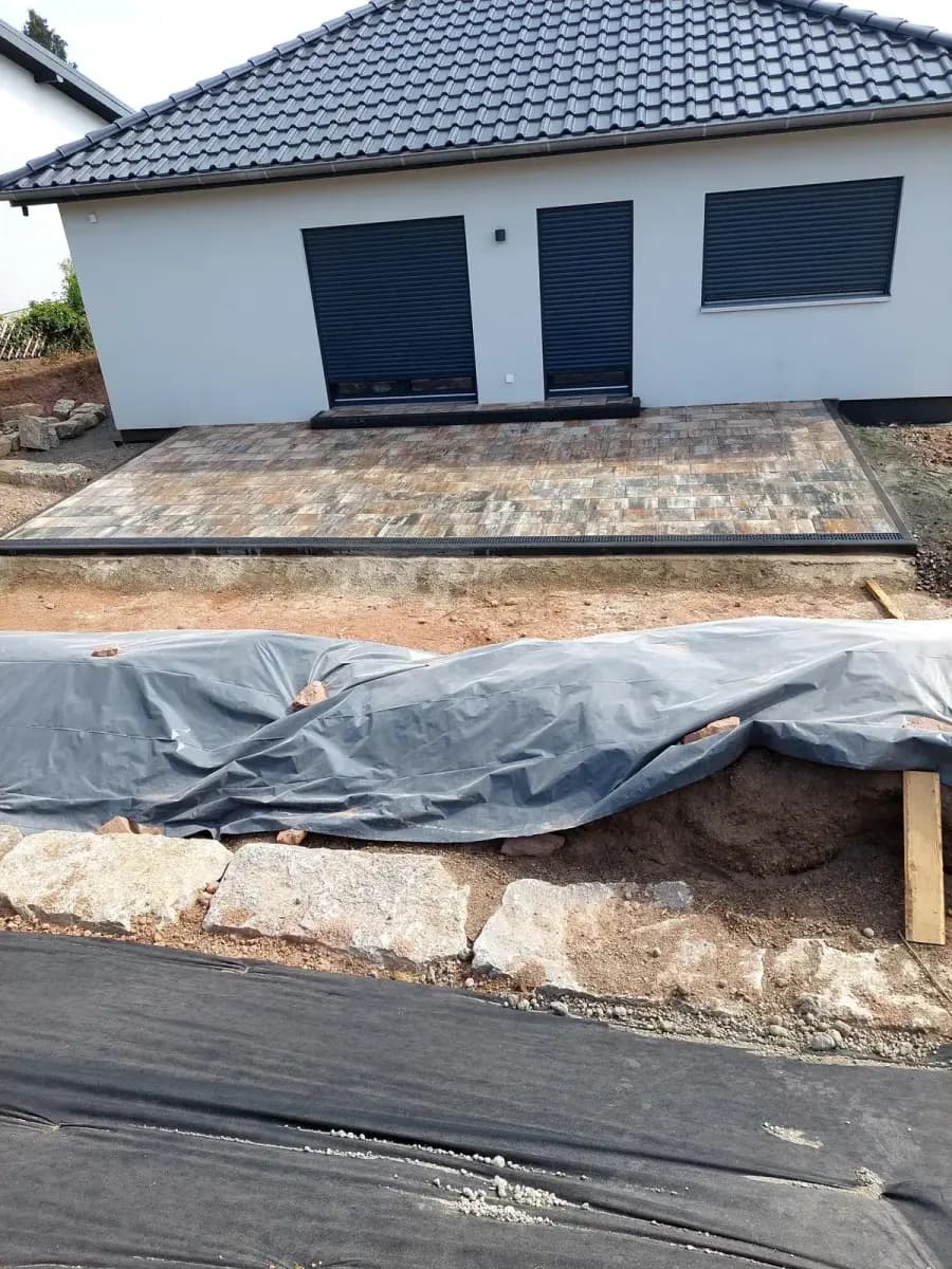Nachher: fertig gepflasterte Terrassenfläche mit Natursteinmauer und modellierter Gartenfläche am Neubau