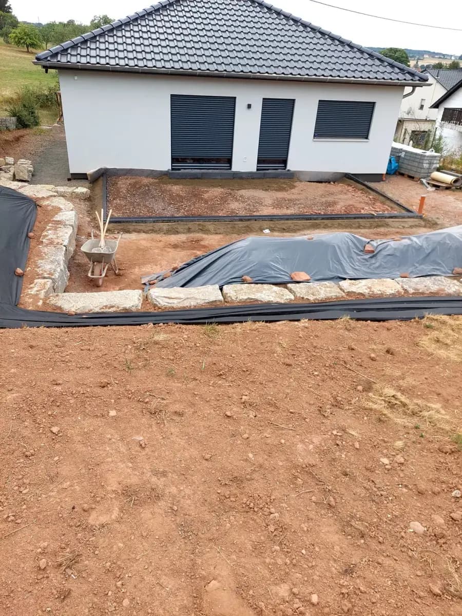 Vorher: Baugrundstück mit Erdarbeiten, Natursteinmauer und vorbereitetem Terrassenunterbau am Neubau